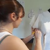 Una de las participantes en el curso pasado ajusta una "toile" a la sisa bajo el brazo y porta un lapicero en su mano derecha para marcar. 